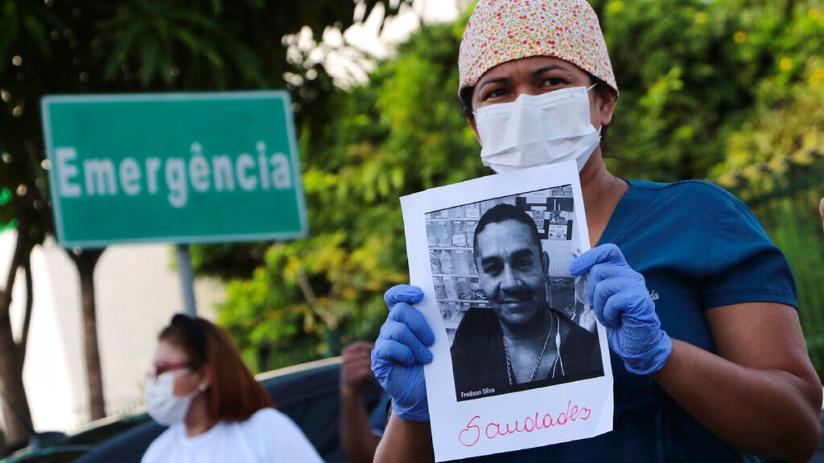 A health worker holds a photo of a person he said was his colleague who died of COVID-19, at a protest outside "Pronto Socorro 28 de Agosto" Hospital in Manaus, Brazil, Monday, April 27, 2020.