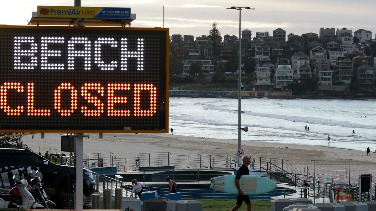 A sign indicates the beach is closed as a surfers arrives for the 7A.M. opening of Bondi Beach in Sydney, Tuesday, April 28, 2020, as coranavirus pandemic restrictions are eased. The beach is open to swimmers and surfers to exercise only.