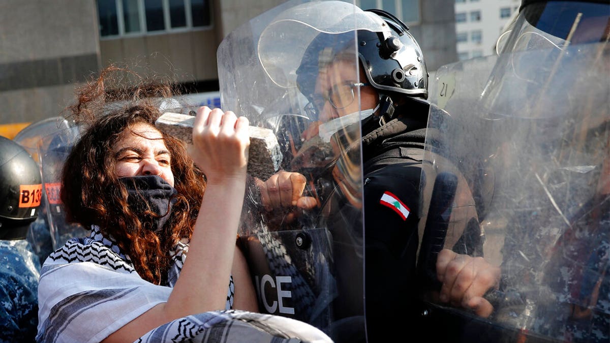 An anti-government protester uses stone to beat on the shield of a riot policeman, during a protest against the deepening financial crisis, in Beirut, Lebanon, Tuesday, April 28, 2020. 