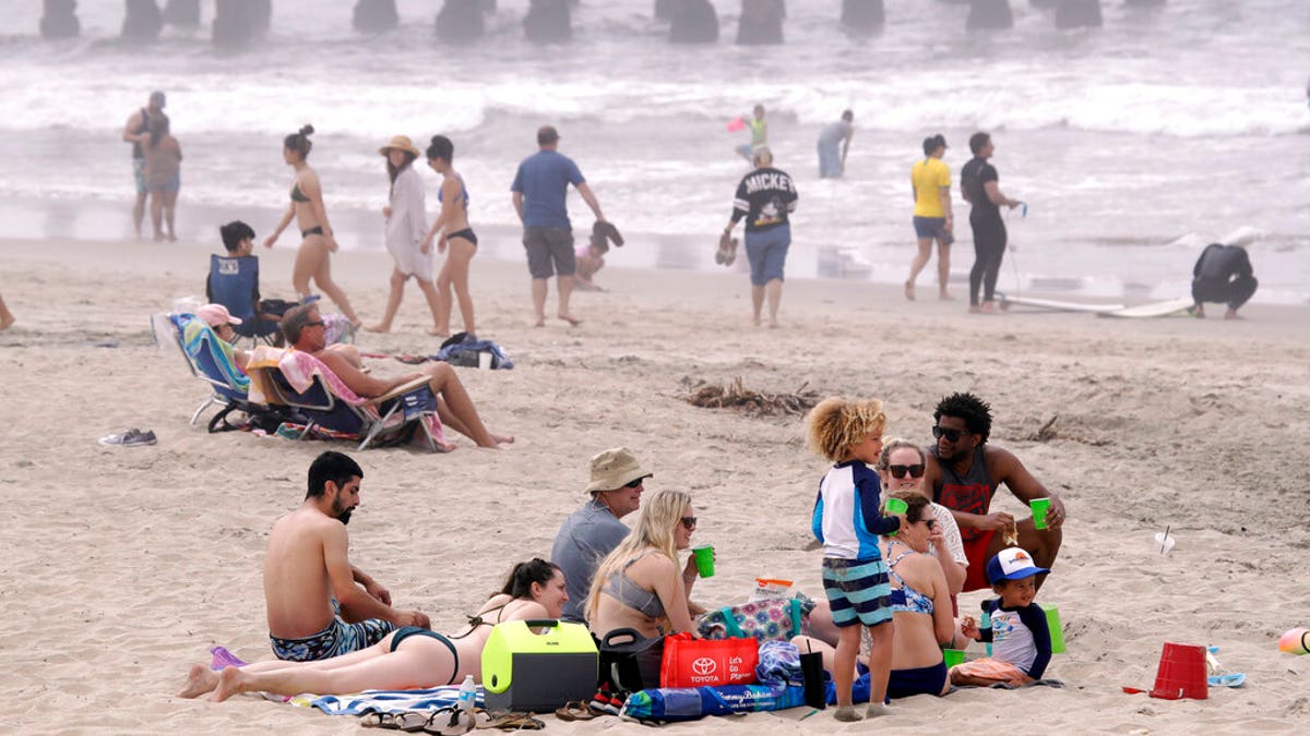 People sit on the beach in Huntington Beach, Calif.