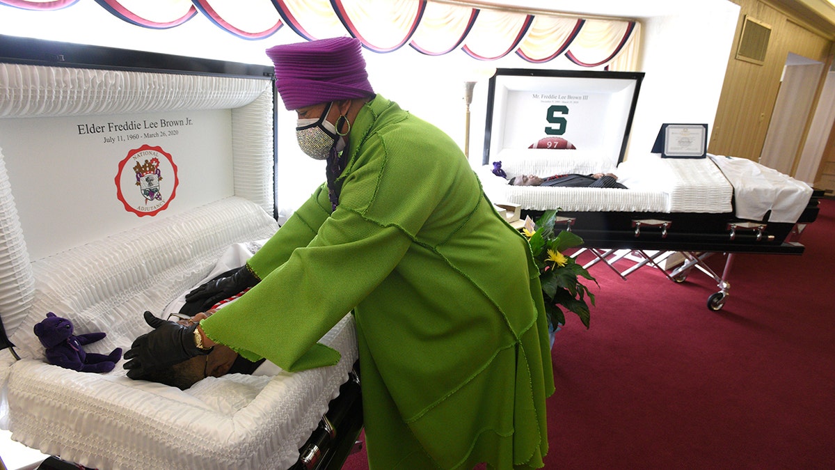 Sandy Brown touching the forehead of her late husband, Freddie Lee Brown, Jr., after she cried over her late son, Freddie Lee Brown, III, right, Friday in Flint, Mich. (Todd McInturf/Detroit News via AP)