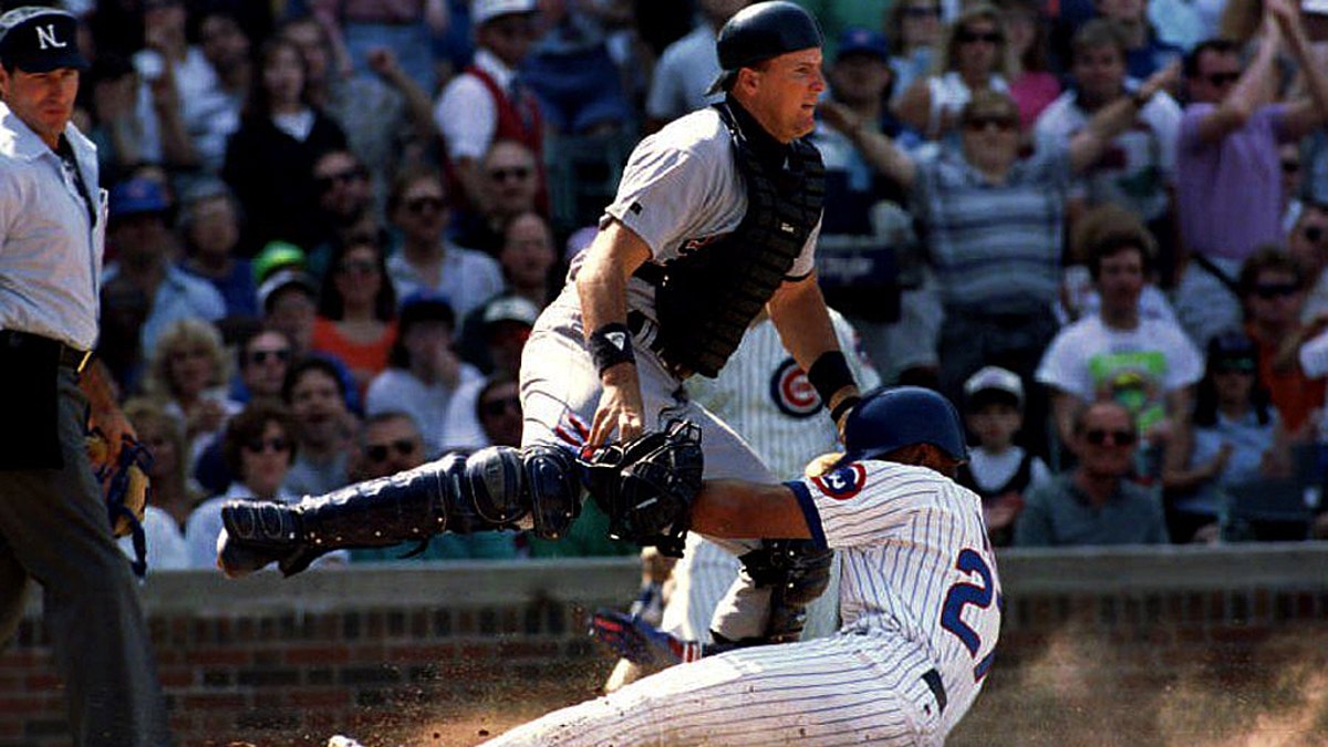 San Diego Padres catcher Dan Walters (C) tries to avoid being run into by sliding Chicago Cub Derrick in May 1993 as he scores in the second inning at Wrigley Field. May scored on a single by Steve Buechele as umpire Angel Hernandez (L) looks on. (Photo credit should read EUGENE GARCIA/AFP via Getty Images)