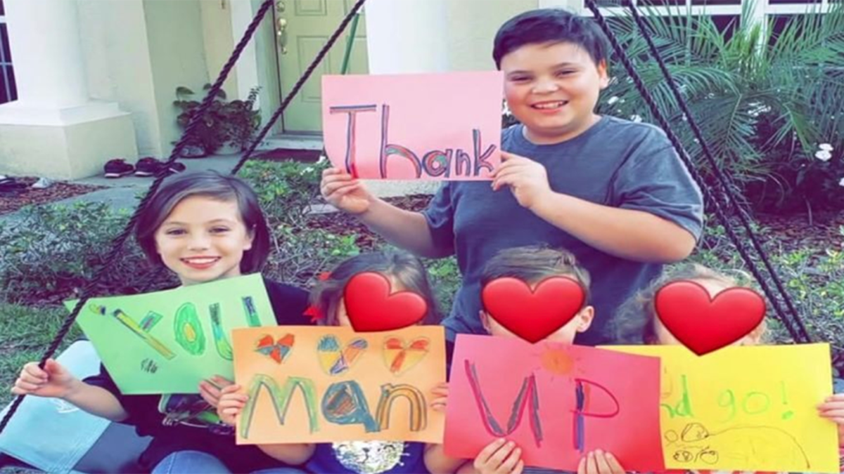 Children hold up "Thank you Man Up" signs after the group has been helping foster families amid the coronavirus pandemic.