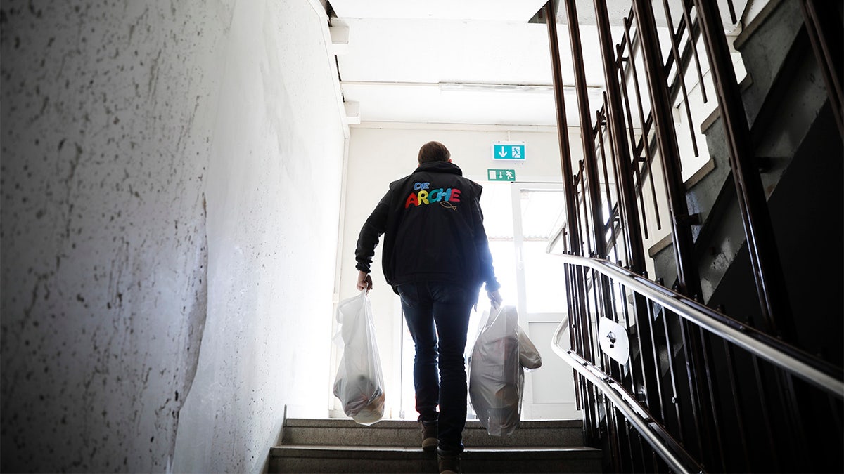 Pastor Bernd Siggelkow founder of the Christian charity the Arche, or Ark, carries bags with donated goods for poor families up the stairs of a center of the organization in Berlin, Germany, Tuesday, March 31, 2020. (AP Photo/Markus Schreiber)