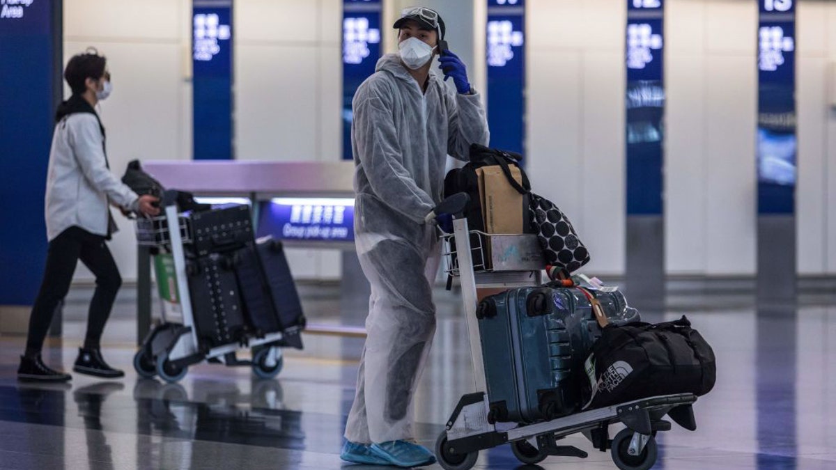A passenger wearing a face mask and protective suit, amid concerns of the COVID-19 coronavirus, talks on his phone in the arrivals hall at Hong Kong International Airport on April 4, 2020. (Photo by DALE DE LA REY/AFP via Getty Images)