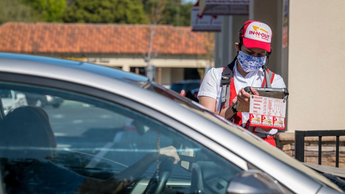 A worker at an In-N-Out restaurant in California is seen wearing a cloth face covering as he takes an order from a customer waiting in a drive-thru line on Tuesday, April 7, 2020.