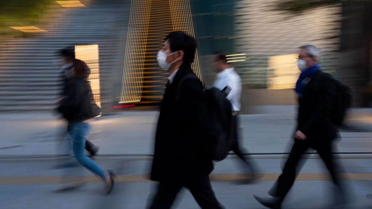 Commuters walk along a sidewalk Monday, April 6, 2020, in Tokyo.