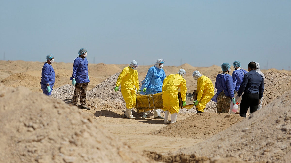 FILE - In this March 30 photo, Iraqi health ministry workers carry a coffin of a person who died from coronavirus at a new cemetery for the people who died from Covid-19 outside the town of Najaf, Iraq. Across the Middle East and parts of South Asia, bereaved families have faced traumatic restrictions on burying their dead amid the pandemic. Religion and customs that require speedy burials in the largely Muslim region have clashed with fears of COVID-19 contagion and government-mandated lockdowns. (AP Photo/Anmar Khalil, File)