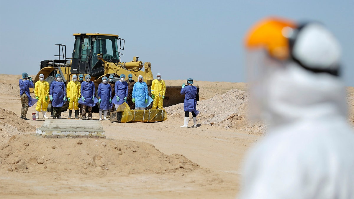 File - In this March 30 photo, Iraqi health ministry workers pray by a coffin of a person who died from coronavirus at a new cemetery for the people who died from Covid-19 outside the town of Najaf, Iraq. Across the Middle East and parts of South Asia, bereaved families have faced traumatic restrictions on burying their dead amid the pandemic. Religion and customs that require speedy burials in the largely Muslim region have clashed with fears of COVID-19 contagion and government-mandated lockdowns. (AP Photo/Anmar Khalil, File)