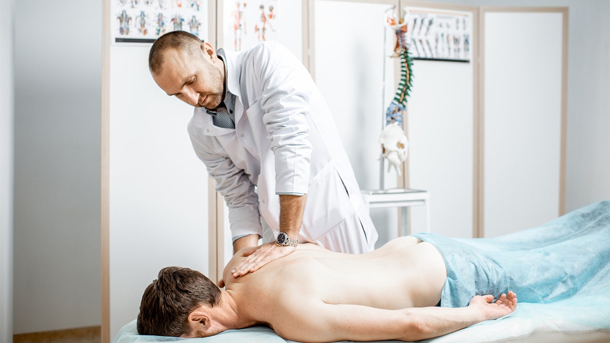 Professional senior physiotherapist doing manual treatment to a men's thoracic spine.