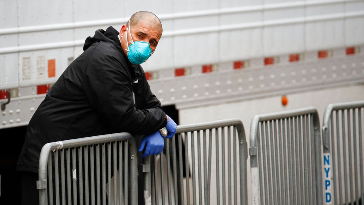 A medical worker wearing personal protective equipment due to COVID-19 concerns rests beside a refrigerated container truck functioning as a makeshift morgue. (AP Photo/John Minchillo)