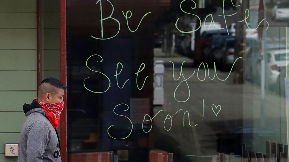 A man wears a bandana on his face as he walks past a sign written on the window of a Starbucks coffee shop, which was closed for coronavirus concerns, in San Francisco, Tuesday, March 24, 2020. (AP Photo/Jeff Chiu)