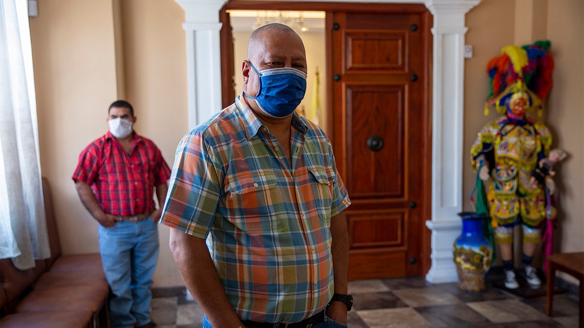 In this April 3, 2020 photo, Mayor Florencio Carrascoza Gámez, wearing a protective mask, poses for photos at his office in the largely indigenous town of Joyabaj, Guatemala, where half of the residents depend on remittances, almost all from the U.S.  (AP Photo/Moises Castillo)