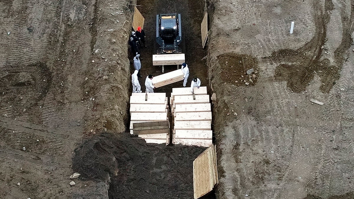 Workers wearing personal protective equipment bury bodies in a trench on Hart Island in New York City's Bronx borough on Thursday. (AP)