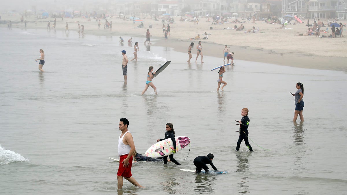 Swimmers and surfers wade in the water Sunday, April 26, 2020, in Newport Beach, Calif. A lingering heat wave lured people to California beaches, rivers and trails again Sunday, prompting warnings from officials that defiance of stay-at-home orders could reverse progress and bring the coronavirus surging back. (AP Photo/Marcio Jose Sanchez)