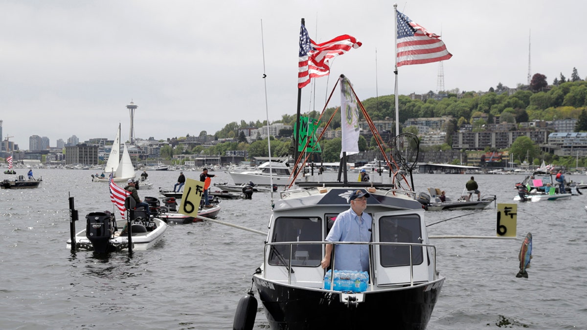A protester reels in a fake fish near poles marking a six-foot social distance on a boat on Lake Union near Gas Works Park in Seattle on April 26. (AP Photo/Ted S. Warren)