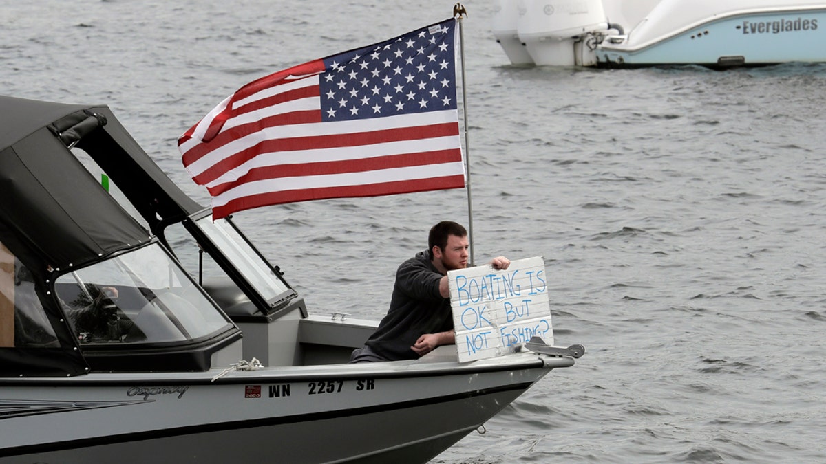 A protester hold a sign that reads "Boating is OK, but Not Fishing?" as he sits on a boat on Lake Union near Gas Works Park in Seattle on April 26. (AP Photo/Ted S. Warren)