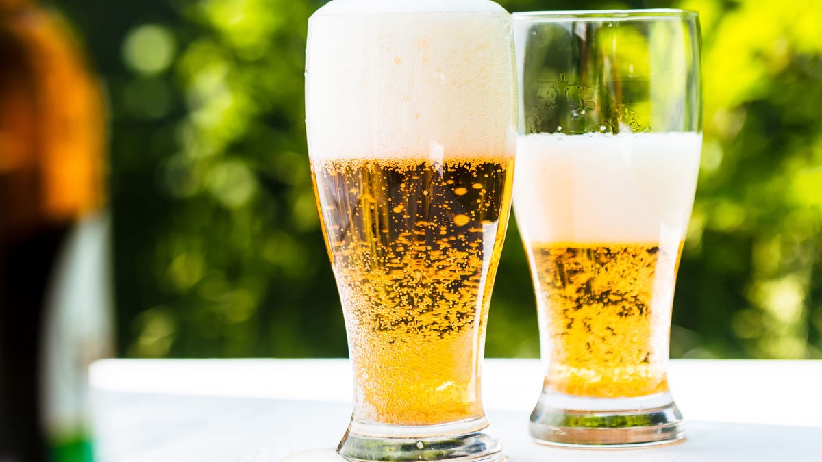 Two glasses of beer on a white wooden table.