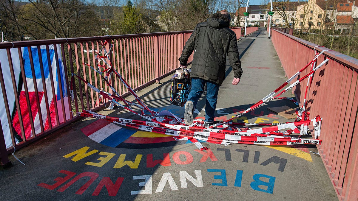 A man with a shopping bag crosses the cordoned off friendship bridge between the villages of Grosbliederstroff in France and Kleinblittersdorf in Germany.(Oliver Dietze/dpa via AP)