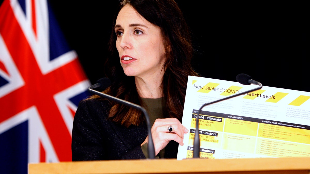 New Zealand Prime Minister Jacinda Ardern holds up a card showing a new alert system for COVID-19. (AP)