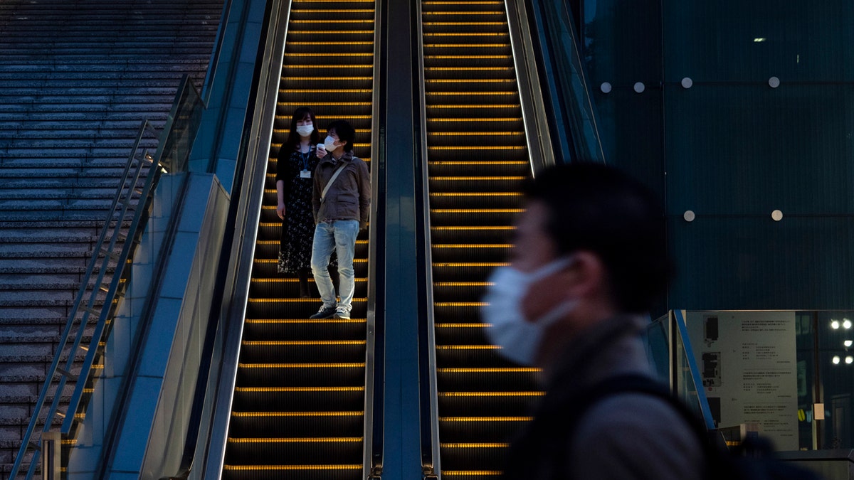 Wearing protective masks to help reduce the spread of the coronavirus, commuters ride an escalator Monday, April 6, 2020, in Tokyo.