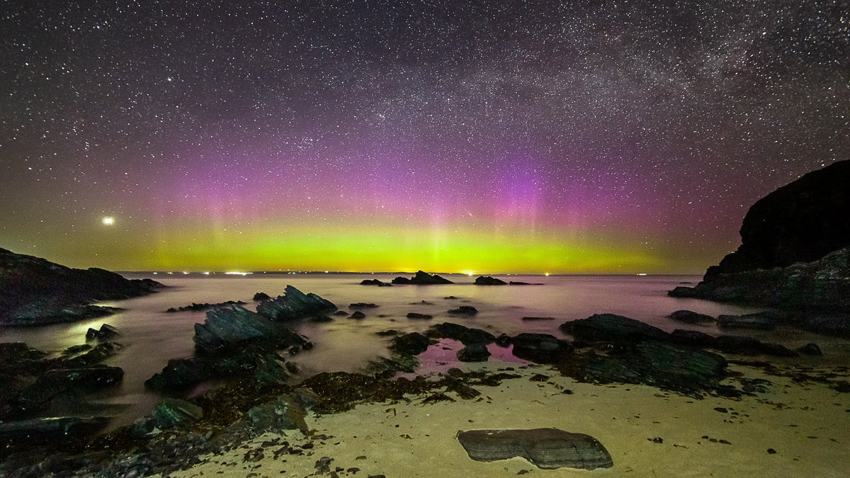 Bright purple and green aurora shine under the Milky Way at Noss Head near Wick in Scotland.