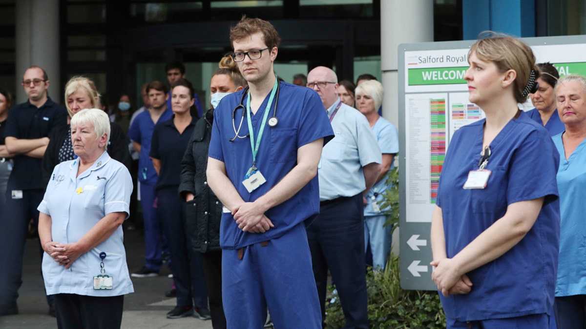 Staff stand outside Salford Royal Hospital in Manchester, England, Tuesday April 28, 2020, during a minute's silence to pay tribute to the NHS staff and key workers who have died during the coronavirus outbreak. (Peter Byrne/PA via AP)