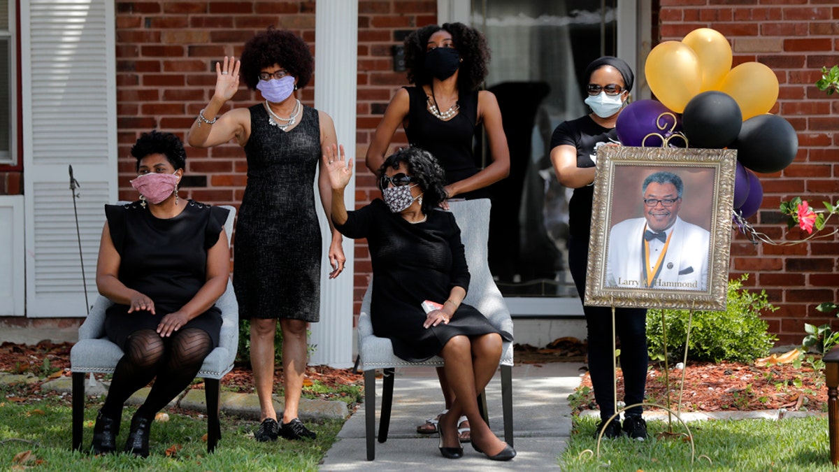 The family of Larry Hammond wave as a line of cars with friends and family, who could not attend his funeral because of limits of gatherings of more than 10 people, due to the coronavirus pandemic, pass by their home, in New Orleans, April 22. (AP Photo/Gerald Herbert)