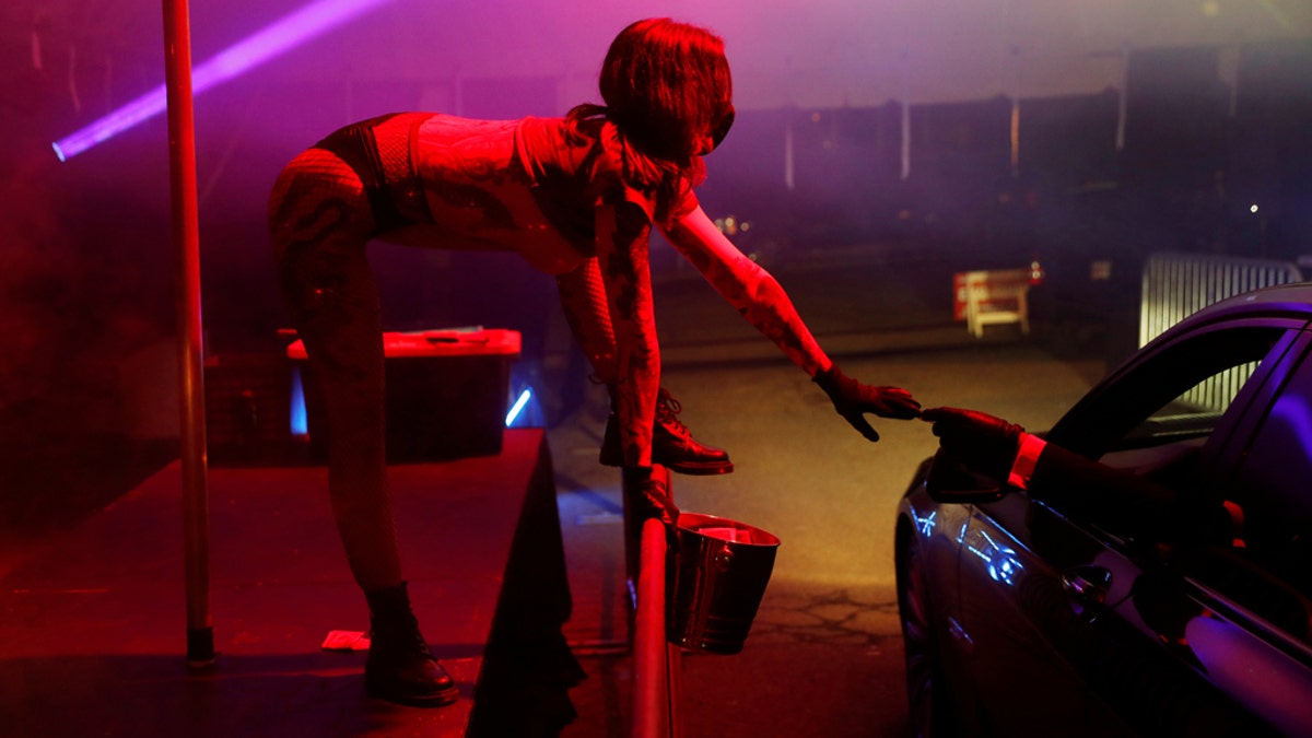 An exotic dancer wears personal protective equipment while taking a tip in a drive-through go-go dance tent at the Lucky Devil Lounge strip club in Portland