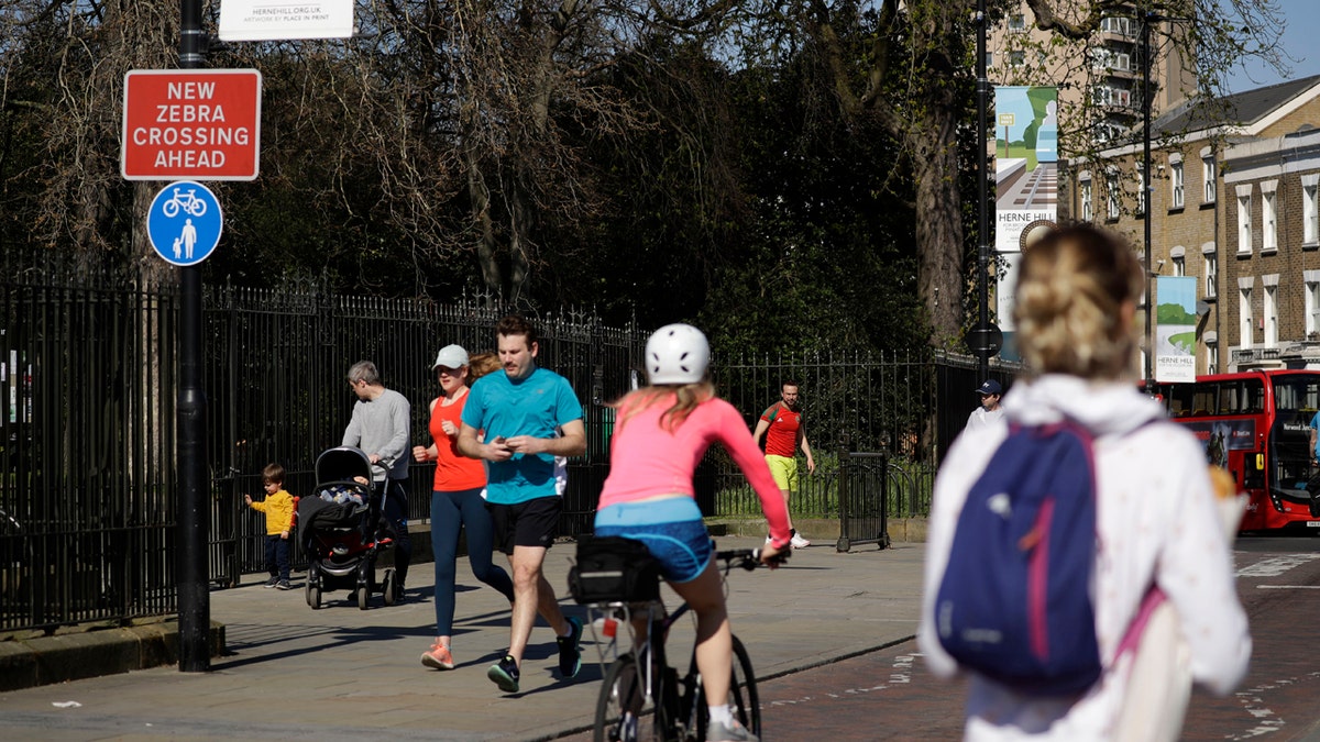 People observe social distancing as they pass by the locked gates to Brockwell Park in London after it was closed overnight to help stop the spread of coronavirus.