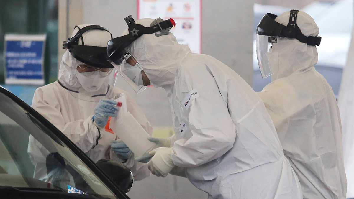 In this March 1, 2020 file photo, medical staff wearing protective suits take samples from a person with suspected symptoms of the new coronavirus at a drive-thru virus test facility in Goyang, South Korea.
