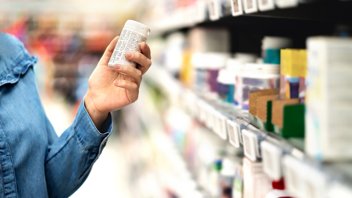 Customer in pharmacy holding medicine bottle. Woman reading the label text about medical information or side effects in drug store. Patient shopping pills for migraine or flu. Vitamin or zinc tablets.