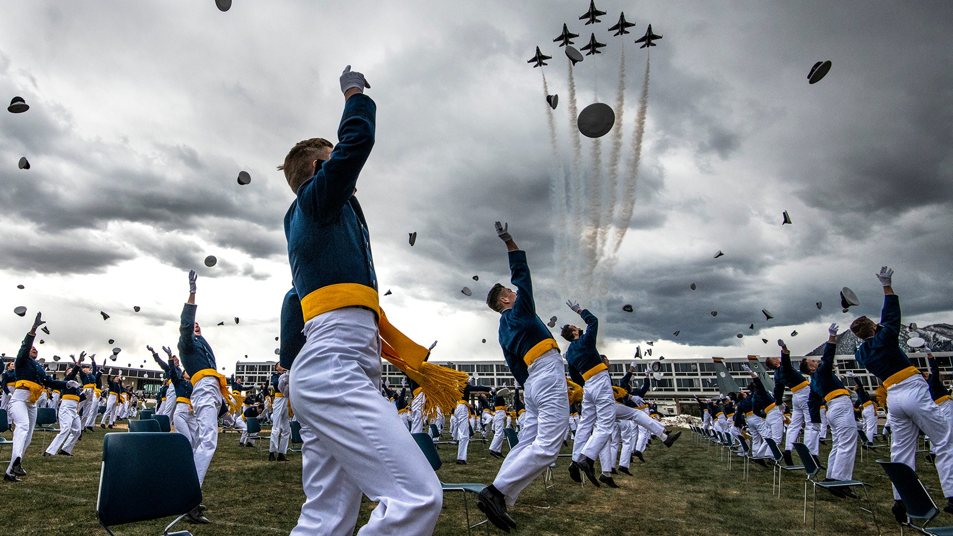 Spaced eight feet apart, United States Air Force Academy cadets celebrate their graduation as a team of F-16 Air Force Thunderbirds fly over the academy in Colorado Springs, Colorado, April 18, 2020.