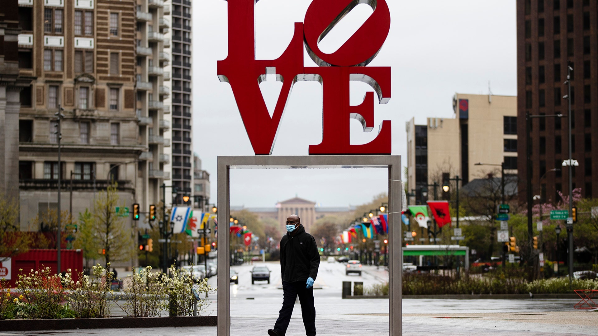 A person wearing a protective face mask and gloves as a precaution against the coronavirus walks by the Robert Indiana sculpture "LOVE" at John F. Kennedy Plaza in Philadelphia, April 13, 2020.