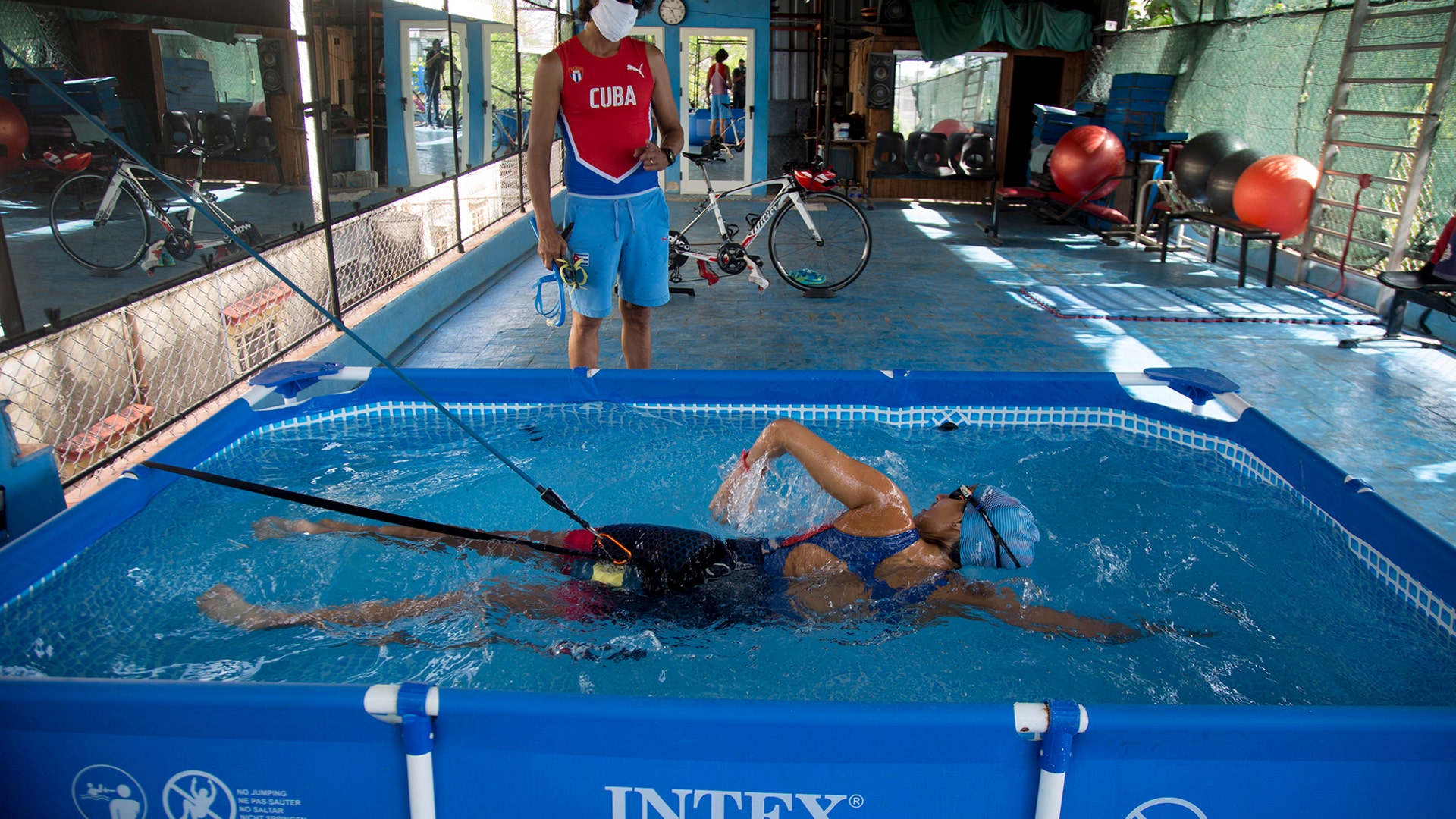 Leslie Amat, a Cuban triathlon athlete, swims in a pool with straps that keep her from advancing, under the watch of her trainer Dioseles Fernandez in the patio of her home in Havana, Cuba, April 20, 2020. 