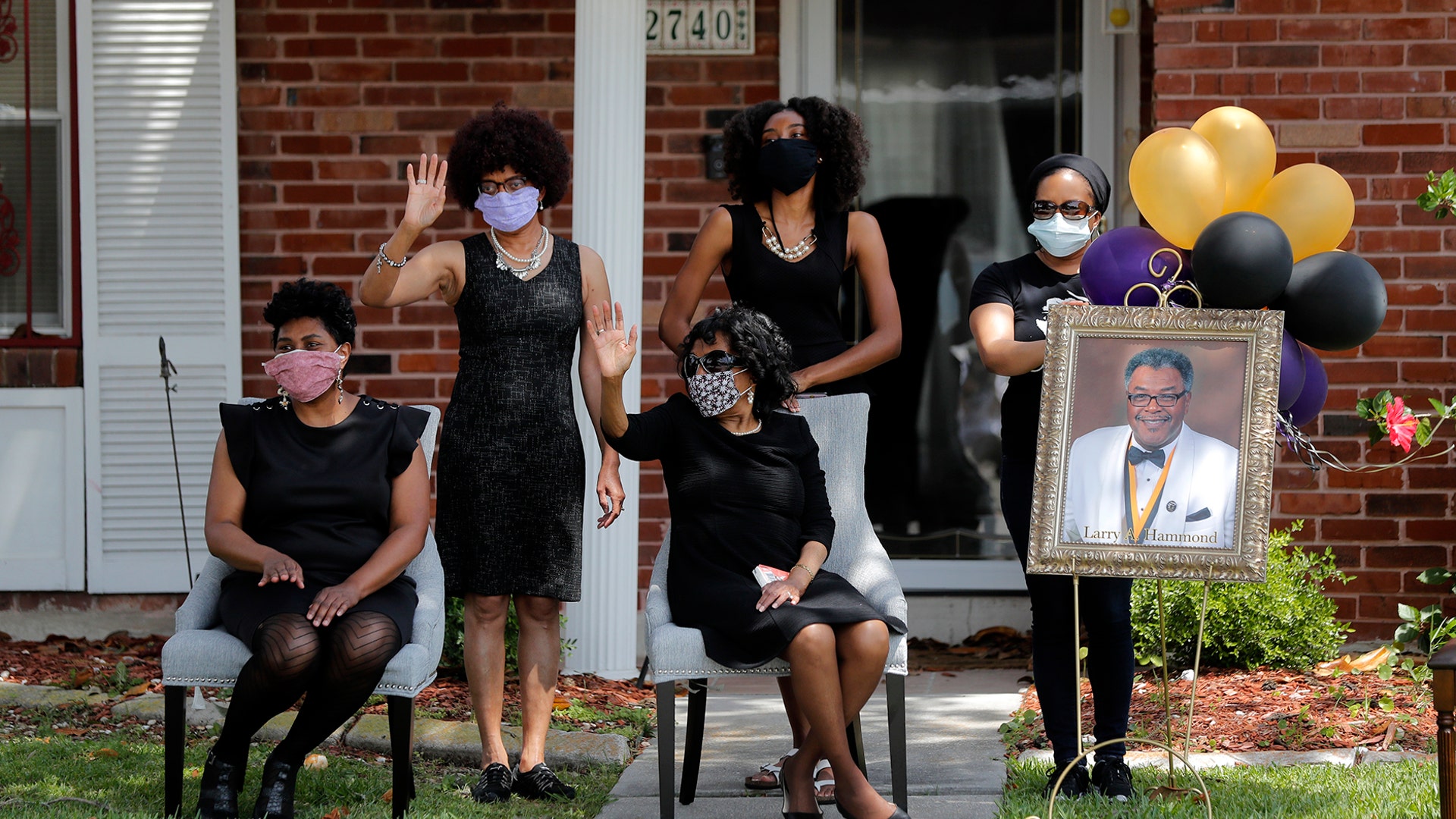 The family of Larry Hammond wave as a line of cars with friends and family, who could not attend his funeral because of limits of gatherings of more than 10 people, due to the coronavirus pandemic, pass by their home, in New Orleans, April 22, 2020.