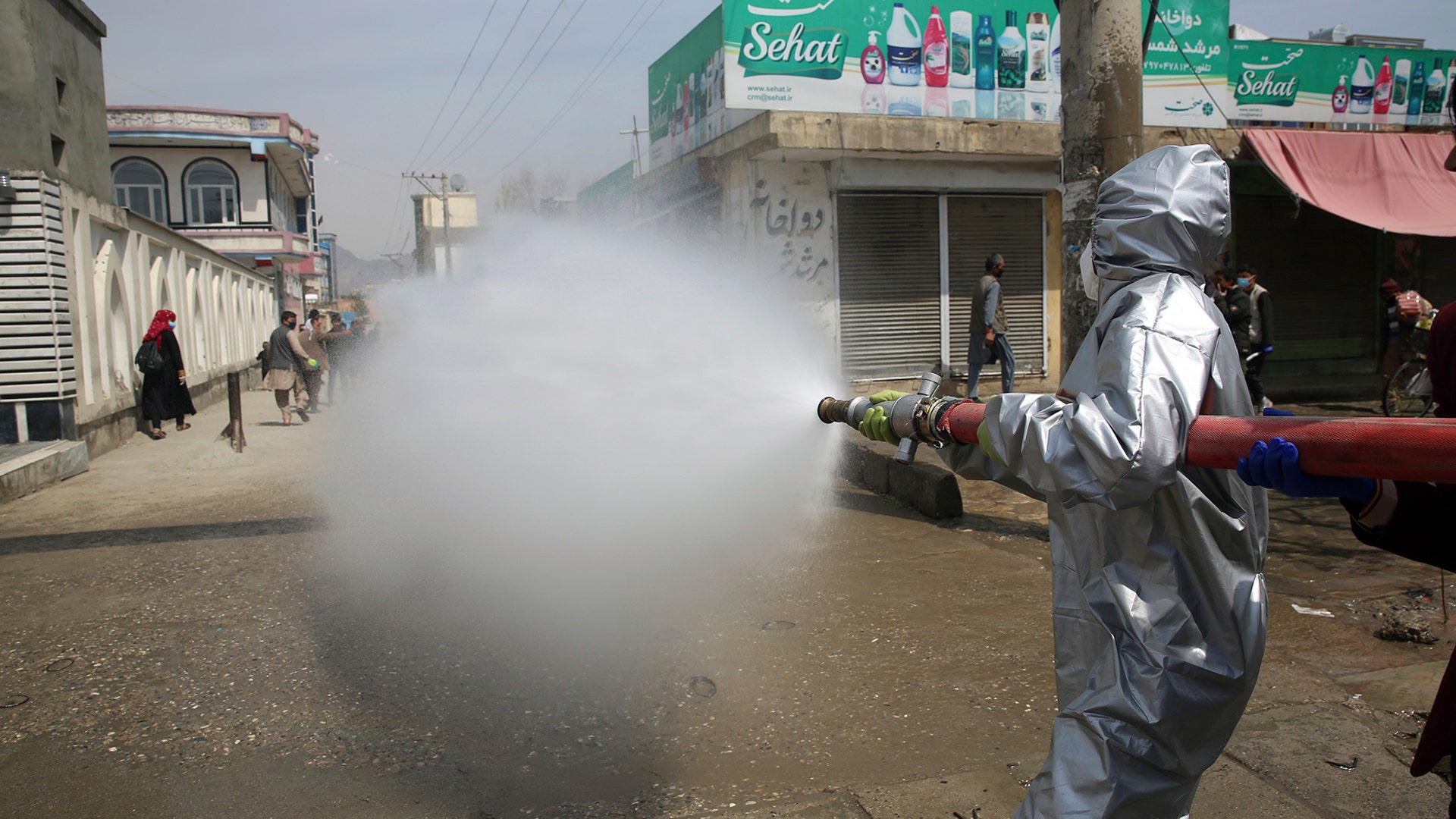 Volunteers and municipality workers in protective suits spray disinfectant along a street to help curb the spread coronavirus in Kabul, Afghanistan, April 8, 2020.