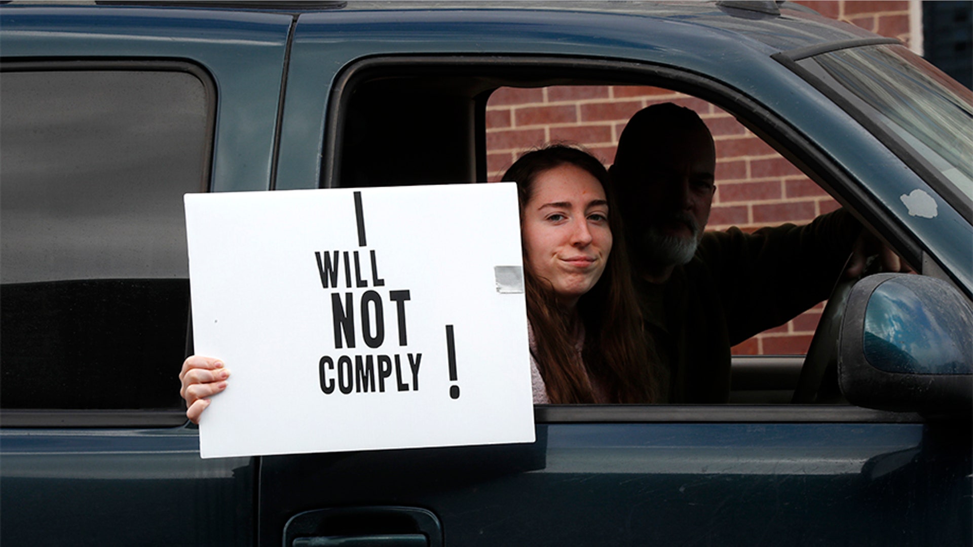 A passenger in a vehicle holds a sign during the protest at the State Capitol in Lansing, Michigan.