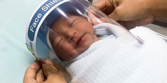 A nurse adjusts a tiny face shield for a newborn baby to protect from new coronavirus at the newborn nursery of the hospital in Samutprakarn province, central Thailand on April 3, 2020. (Paolo Hospital Samutprakarn via AP)