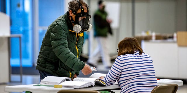 Robert Forrestal, left, wears a full face chemical shield to protect against the spread of coronavirus, as he votes Tuesday, April 7, 2020, at the Janesville Mall in Janesville, Wis. Hundreds of voters in Wisconsin are waiting in line to cast ballots at polling places for the state's presidential primary election, ignoring a stay-at-home order over the coronavirus threat. (Angela Major/The Janesville Gazette via AP)