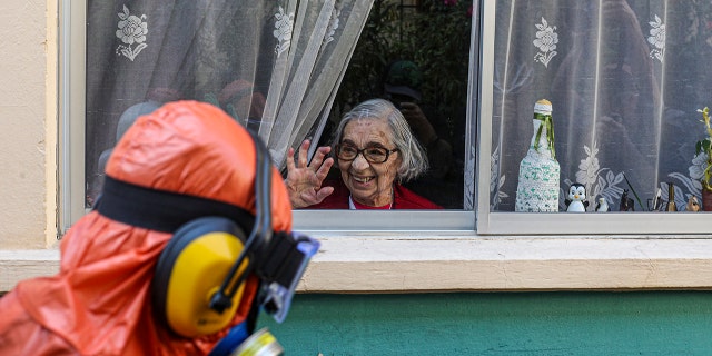 A woman waves to a city worker dressed in a hazmat suit as he disinfects the streets in her neighborhood as a precaution against the spread of the new coronavirus, in Santiago, Chile, Wednesday, April 15, 2020. (AP Photo/Esteban Felix)