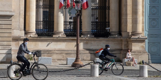 Cyclists wear masks to protect against the spread of the coronavirus ride past a woman who enjoys the sun in front the French parliament in Paris on Sunday. (AP Photo/Michel Euler)