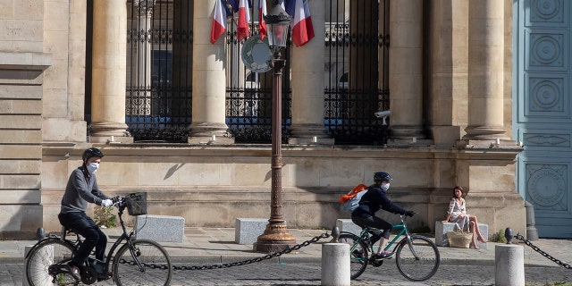 Cyclists wear masks to protect against the spread of the coronavirus ride past a woman who enjoys the sun in front the French parliament in Paris on Sunday. (AP Photo/Michel Euler)