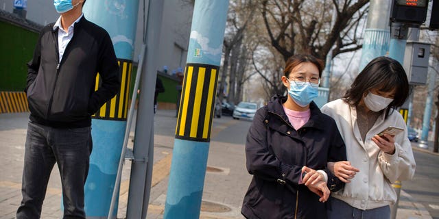 People wearing face masks wait to cross a street in Beijing, on March 31, 2020. China on Tuesday reported just one new death from the coronavirus and a few dozen new cases, all brought from overseas. (AP Photo/Mark Schiefelbein)