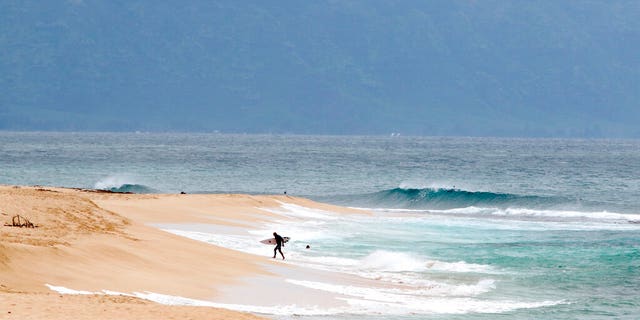 A surfer walks out of the ocean on Oahu's North Shore near Haleiwa, Hawaii, Tuesday, March 31, 2020. The state of Hawaii is reporting its first death of an individual who tested positive for the coronavirus.