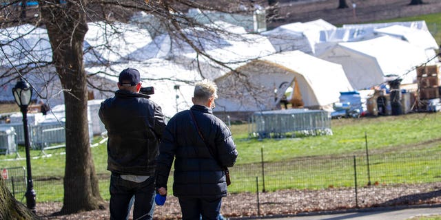 A couple pauses to take a picture of the Samaritan's Purse field hospital as they walk their dog in New York's Central Park, Wednesday, April 1, 2020. The new coronavirus causes mild or moderate symptoms for most people, but for some, especially older adults and people with existing health problems, it can cause more severe illness or death.