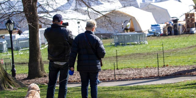 A couple pauses to take a picture of the Samaritan's Purse field hospital as they walk their dog in New York's Central Park, Wednesday, April 1, 2020. The new coronavirus causes mild or moderate symptoms for most people, but for some, especially older adults and people with existing health problems, it can cause more severe illness or death.