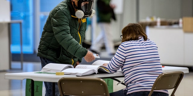 Robert Forrestal, left, wears a full face chemical shield to protect against the spread of coronavirus, as he votes Tuesday, April 7, 2020, at the Janesville Mall in Janesville, Wis. (Associated Press)