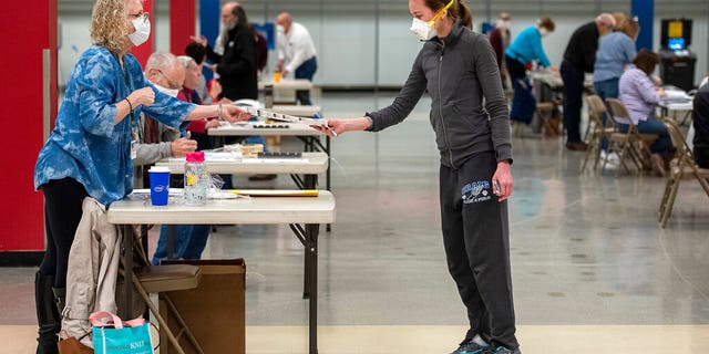 Bridget McDonald, right, receives a ballot from poll worker Patty Piek-Groth on Tuesday, April 7, 2020, at the Janesville Mall in Janesville, Wis. Hundreds of voters in Wisconsin are waiting in line to cast ballots at polling places for the state's presidential primary election, ignoring a stay-at-home order over the coronavirus threat. (Angela Major/The Janesville Gazette via AP)