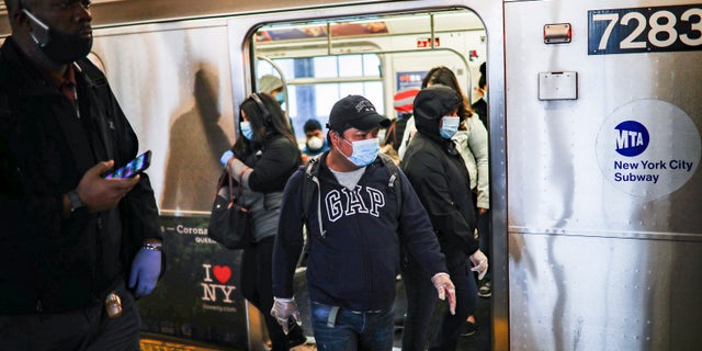 Subway riders, wearing personal protective equipment due to COVID-19 concerns, step off a train, Tuesday, April 7, 2020, in New York.